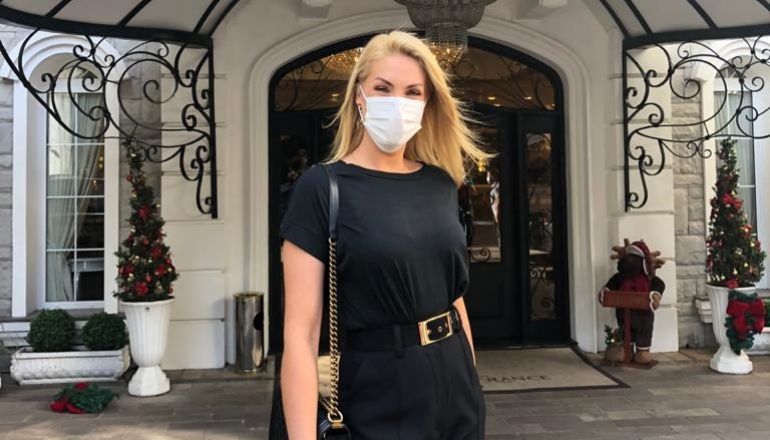 Uma mulher usando uma máscara facial está parada em frente a um prédio.