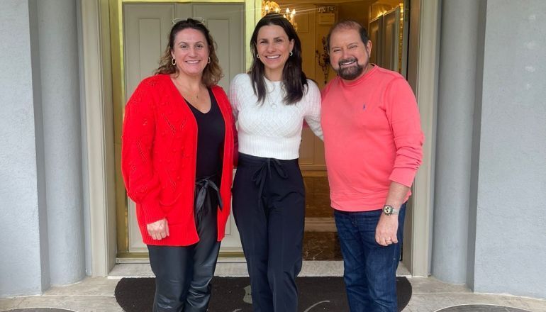 Um homem e duas mulheres posam para uma foto em frente a uma porta.