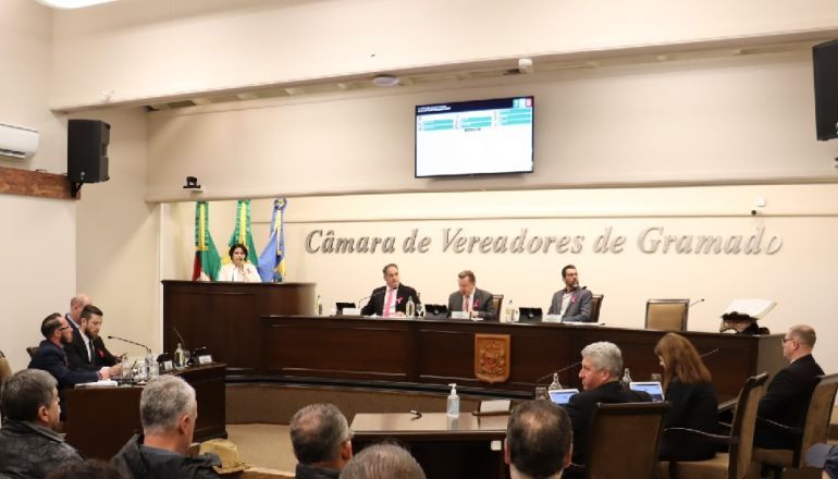 Um grupo de pessoas está sentado à mesa de uma câmara de vereadores de Gramado.
