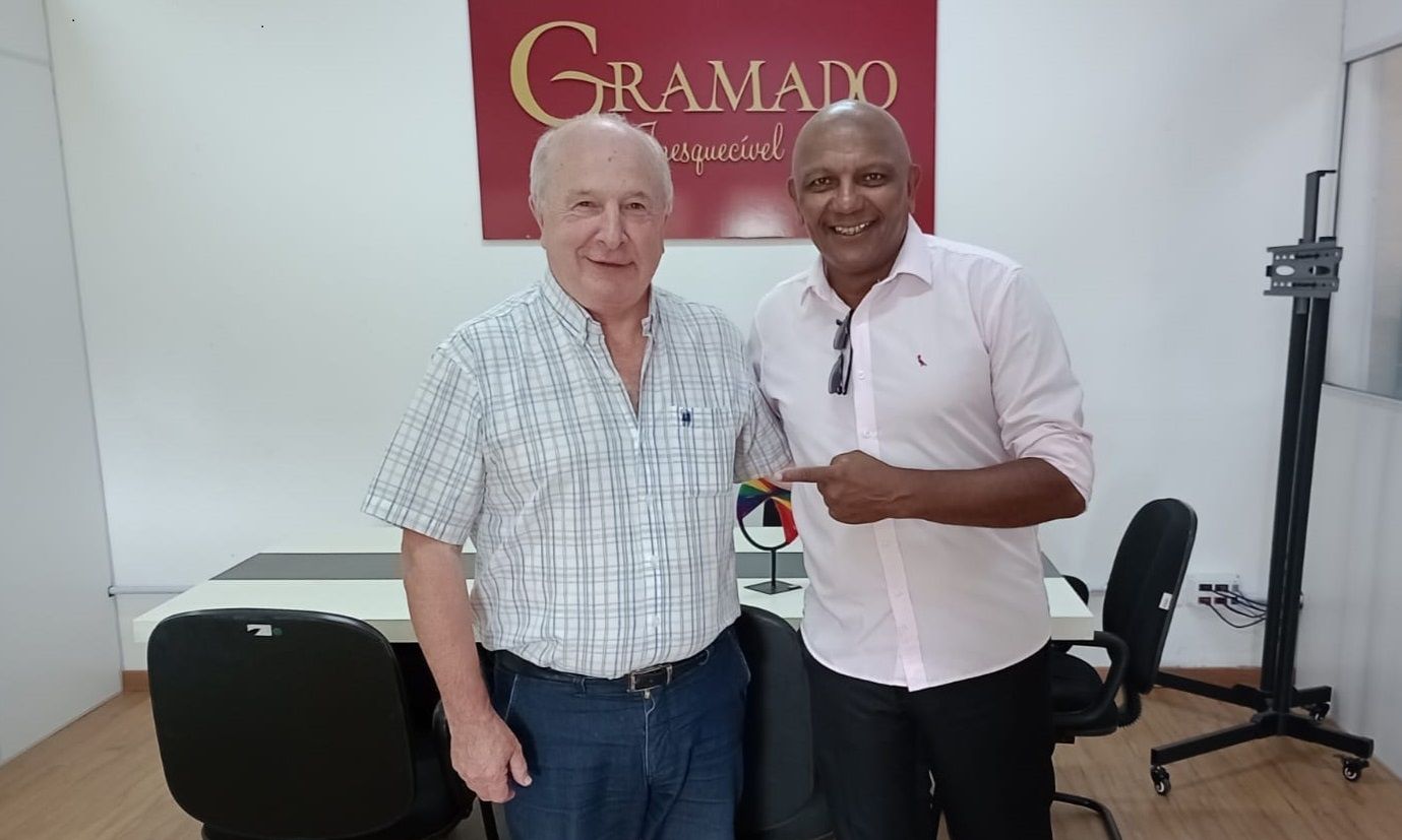 Dois homens estão parados um ao lado do outro em frente a uma placa de Gramado.
