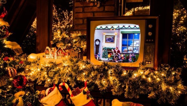 Uma televisão está sobre um manto ao lado de uma árvore de natal.