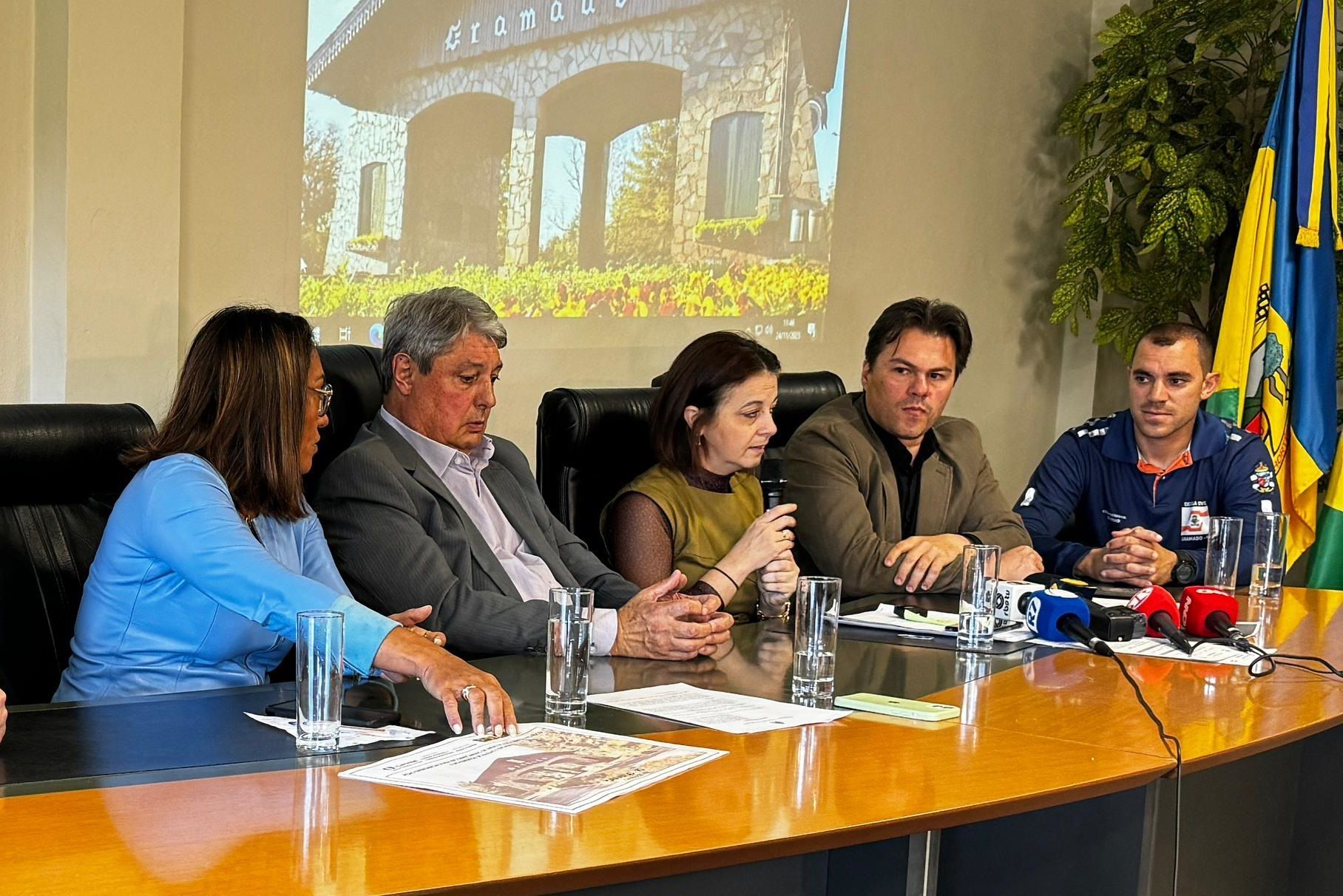Um grupo de pessoas está sentado em uma mesa em frente a uma tela de projetor.