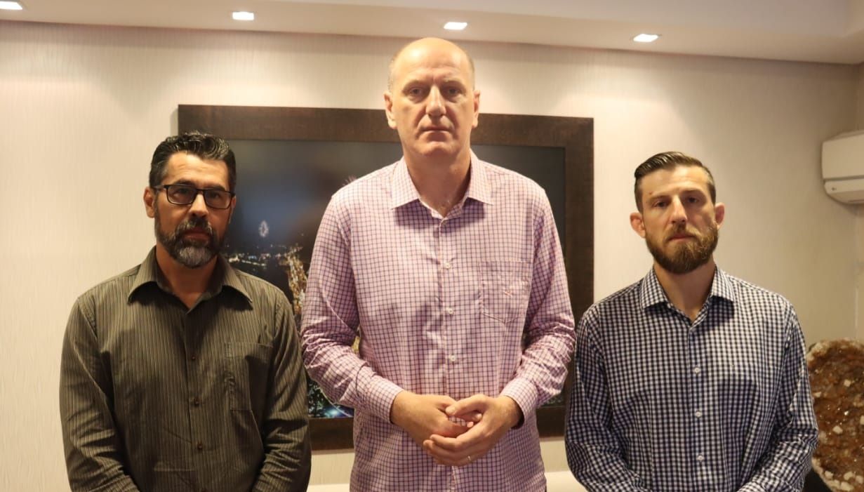 Três homens estão parados um ao lado do outro em uma sala.