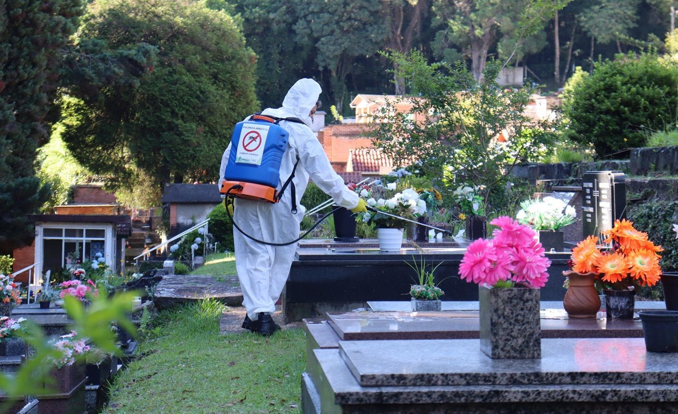 Um homem com traje de proteção está pulverizando flores em um cemitério.