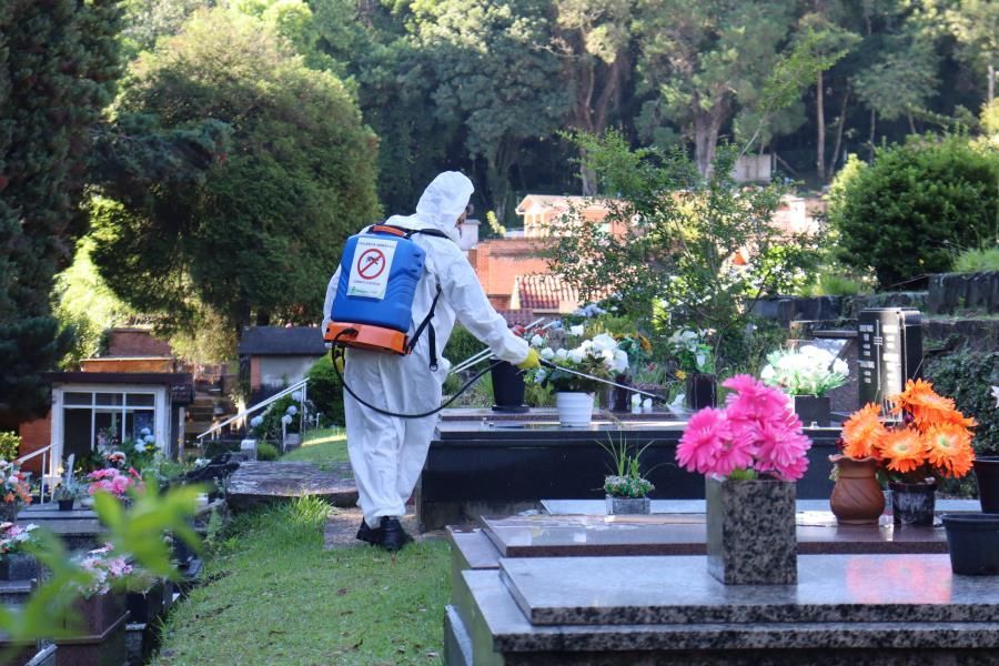 Um homem com traje de proteção está pulverizando flores em um cemitério.