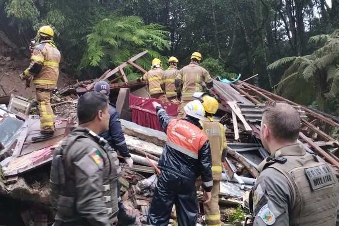 Um grupo de bombeiros e policiais está em volta de uma pilha de escombros.