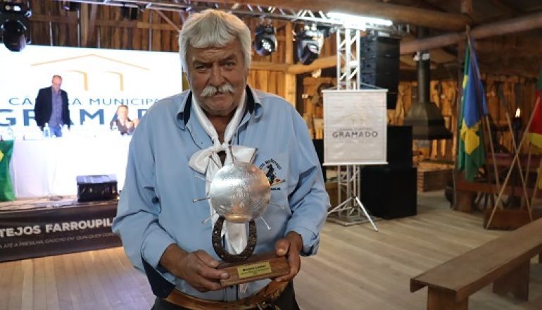 Um homem de bigode segura um troféu em uma sala.