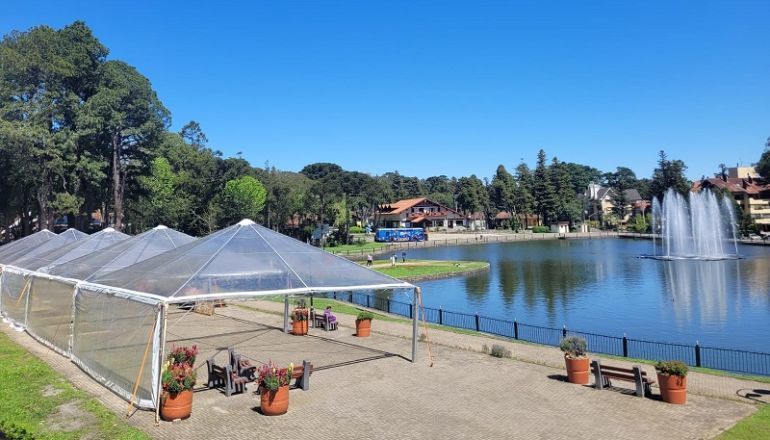 Uma tenda transparente está ao lado de um lago com uma fonte ao fundo.