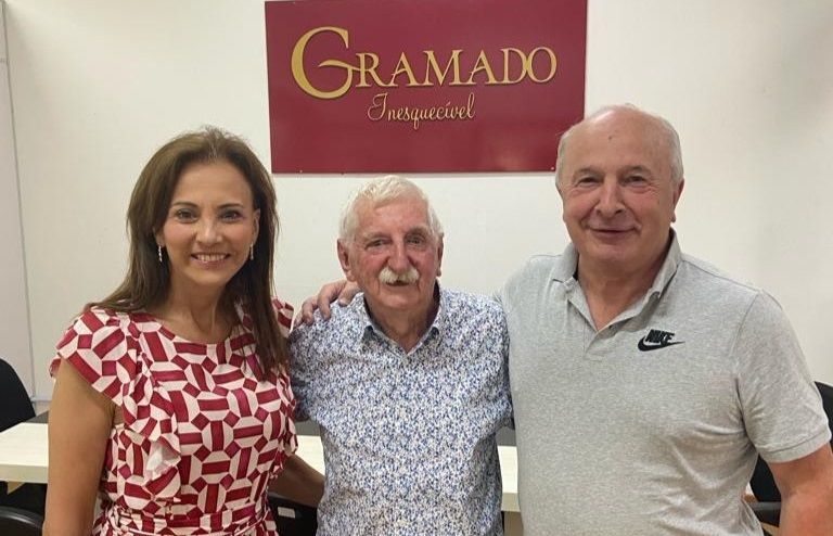 Três pessoas posam para foto em frente a uma placa que diz Gramado