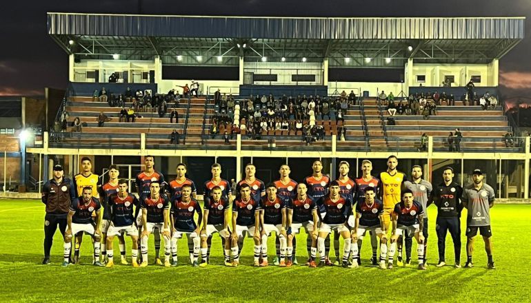 Um grupo de jogadores de futebol está em um campo em frente a um estádio.