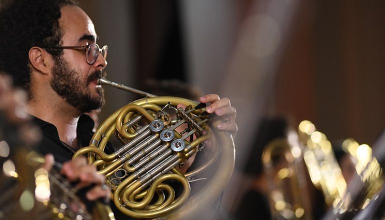 Um homem está tocando trompa em uma orquestra.