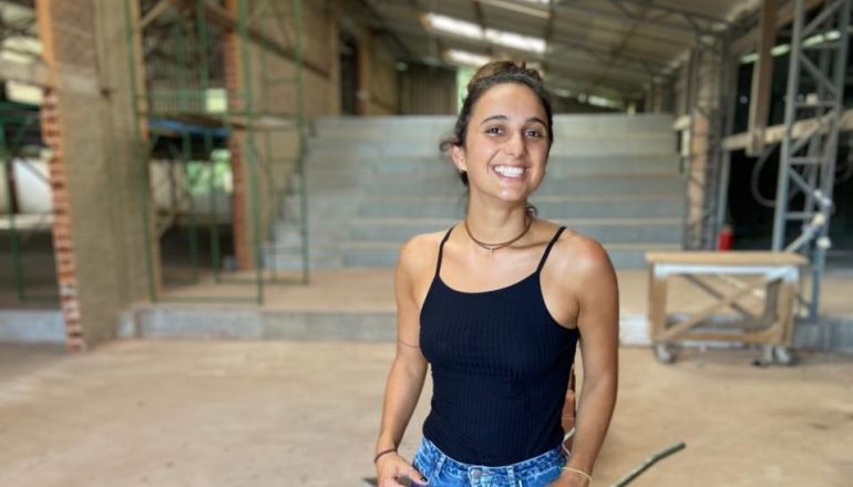 Uma mulher de blusa preta e calça jeans está em um prédio em construção.