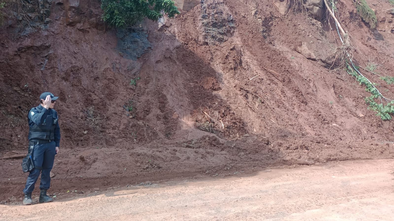 Um policial está parado na frente de uma pilha de terra.