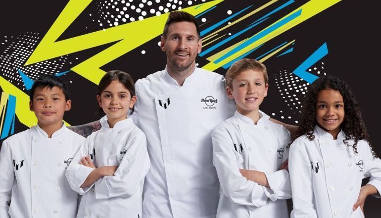 Um grupo de crianças posa para uma foto com um homem com casaco de chef.