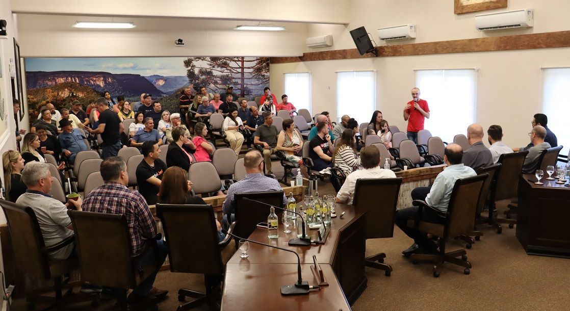 Um grande grupo de pessoas está sentado em uma longa mesa em uma sala de conferências.