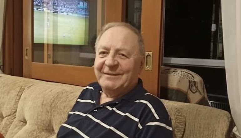 Um idoso está sentado em um sofá em frente a uma televisão.