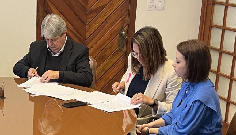 Um homem e duas mulheres estão sentados à mesa assinando papéis.