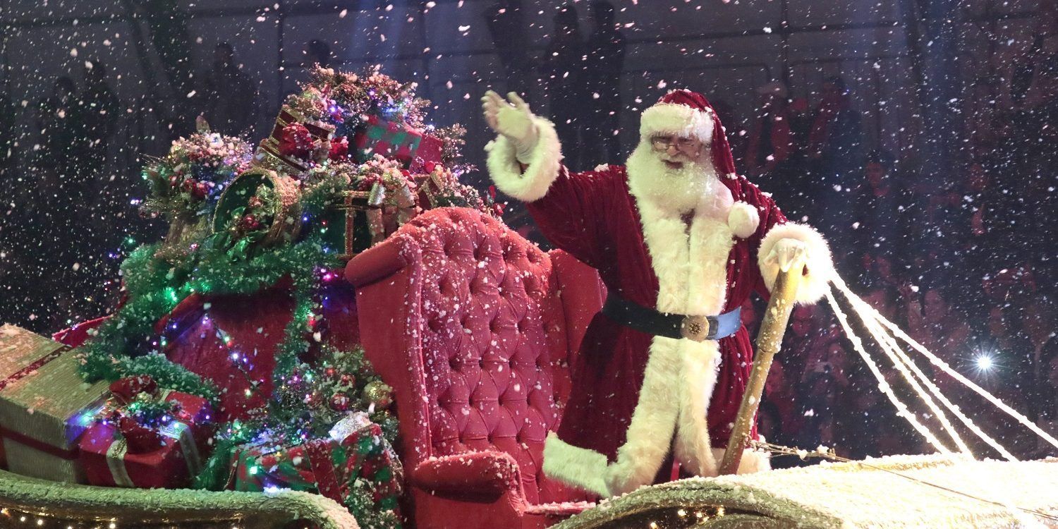 Papai Noel está andando de trenó com uma árvore de Natal ao fundo.
