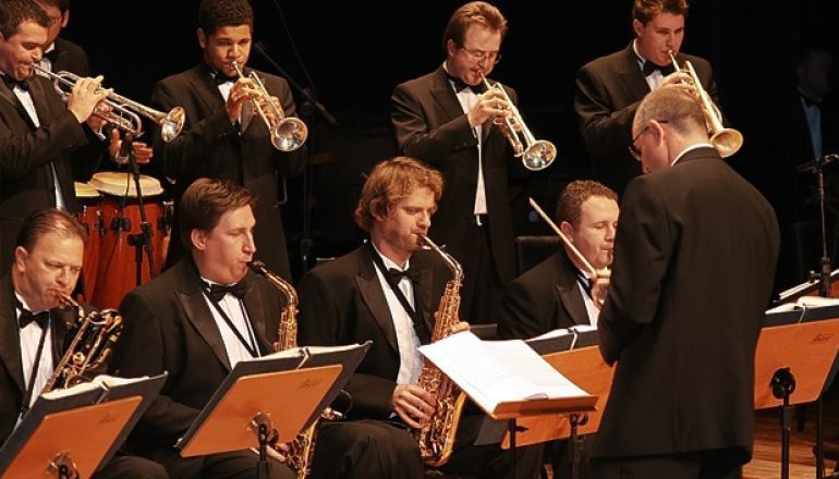 Um grupo de homens de smoking toca instrumentos em um palco