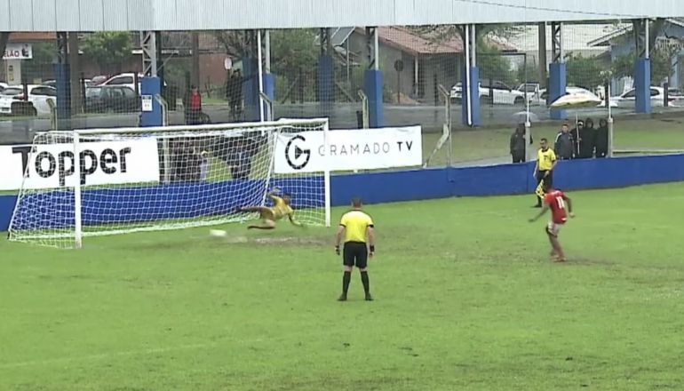 Um grupo de pessoas está jogando futebol em um campo com uma placa de cartola ao fundo.