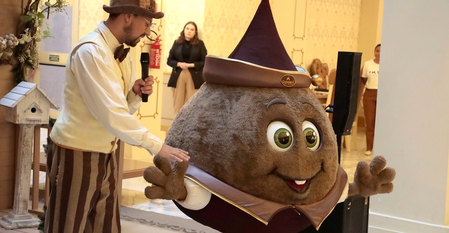 Um homem de cartola está parado ao lado de um mascote.