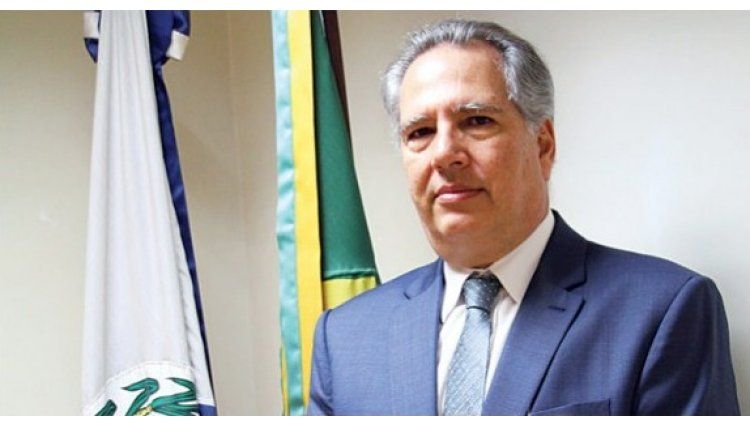 Um homem de terno e gravata está diante de duas bandeiras