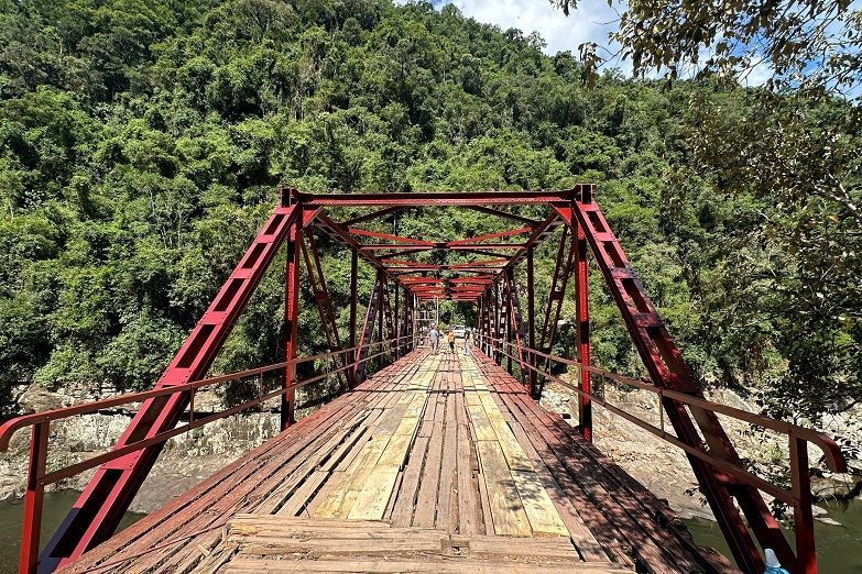 Uma ponte vermelha sobre um rio no meio de uma floresta.