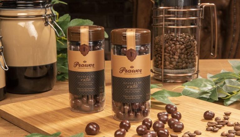 Dois potes de grãos de café com cobertura de chocolate estão sobre uma mesa de madeira.