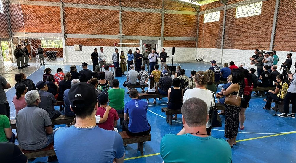 Um grande grupo de pessoas está sentado nos bancos de uma academia.