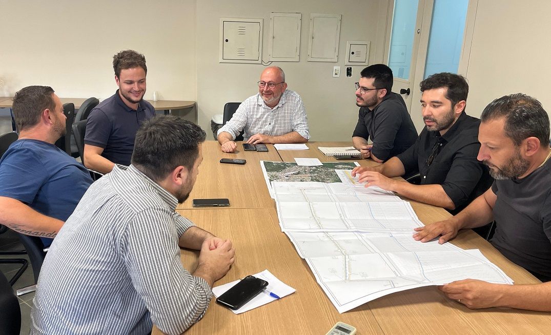 Um grupo de homens está sentado ao redor de uma mesa olhando um mapa.