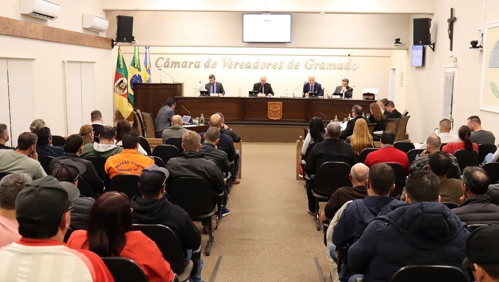 Um grande grupo de pessoas está sentado em frente a um pódio em uma sala.