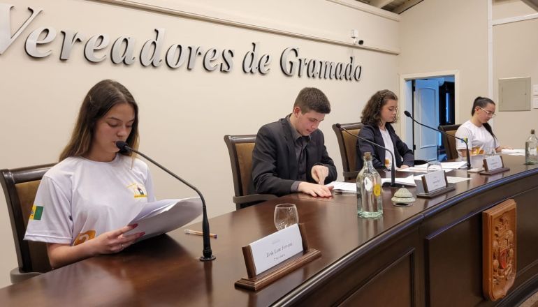 Um grupo de pessoas está sentado em uma mesa em frente a microfones.