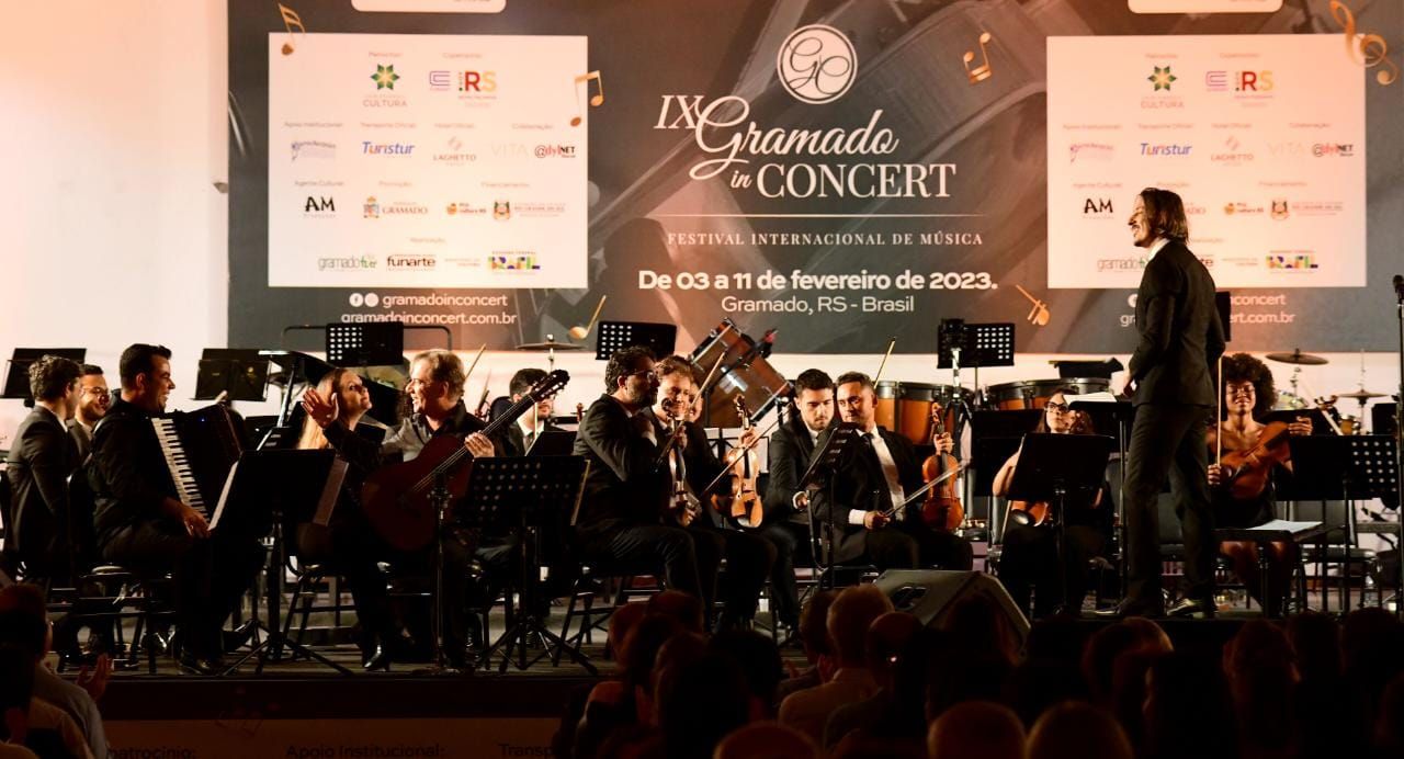 Um homem está diante de uma orquestra em um palco.