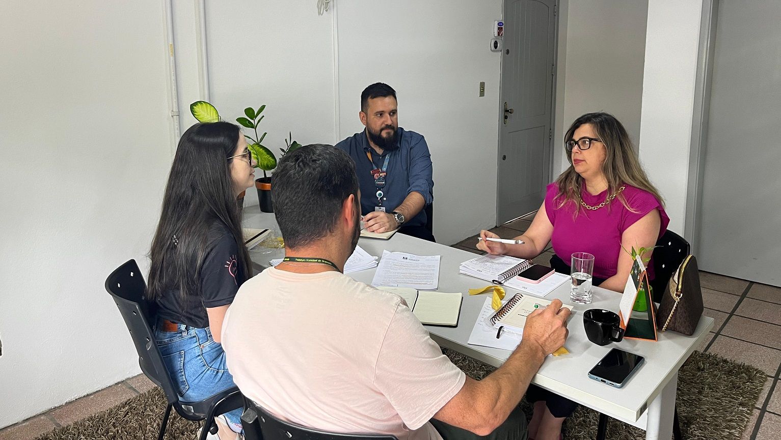 Um grupo de pessoas está sentado ao redor de uma mesa em uma reunião.