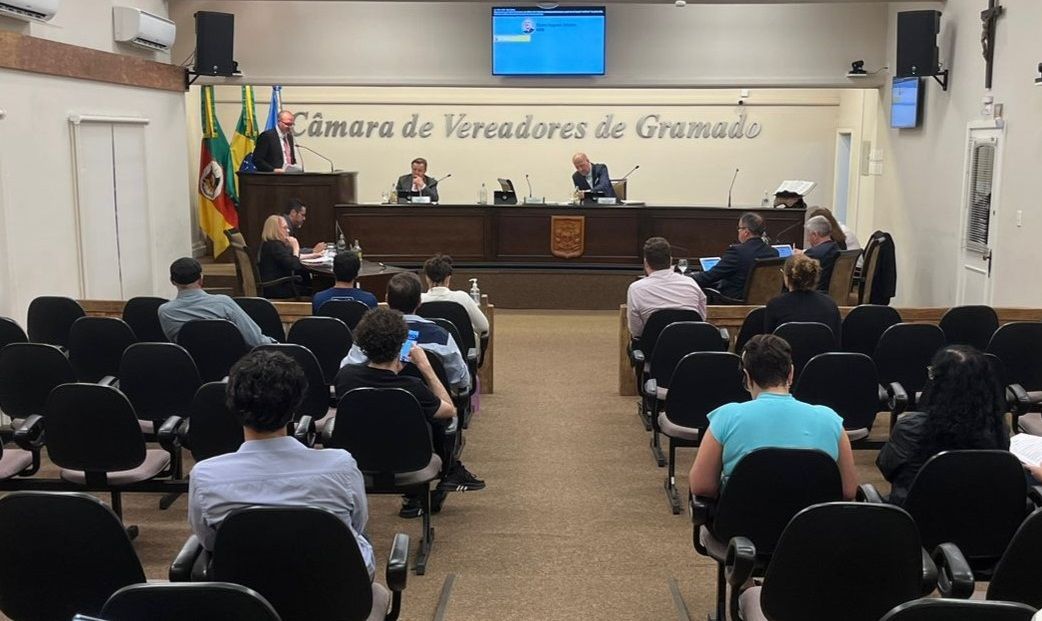 Um grupo de pessoas está sentado em cadeiras em frente a um pódio em uma sala.