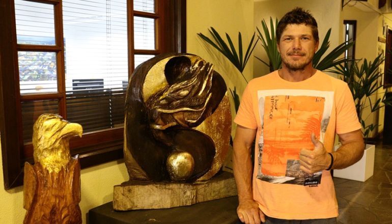 Um homem está parado na frente de uma estátua e levantando o polegar.