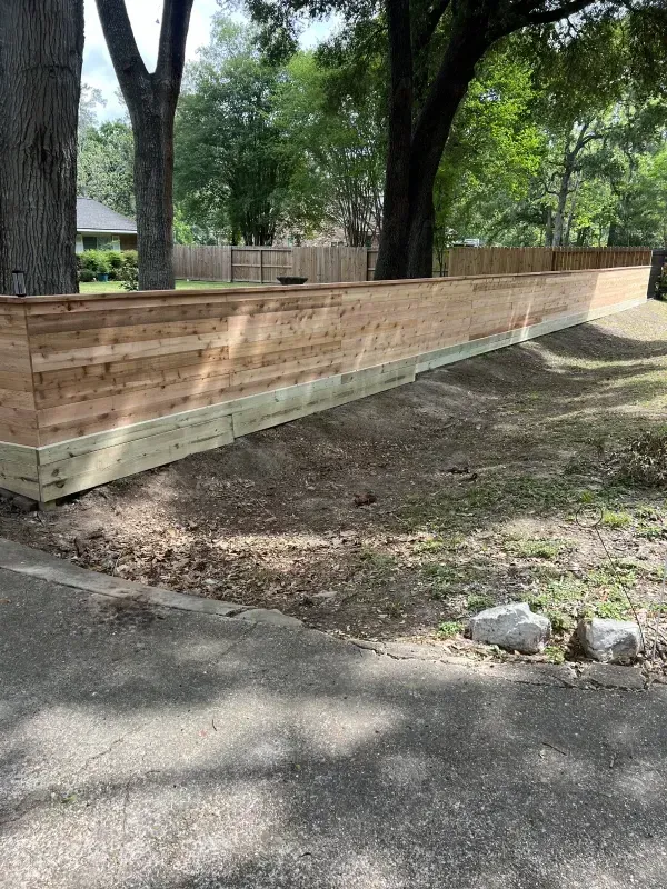 A wooden fence extends along a slightly elevated area, with trees in the background, set on grass.