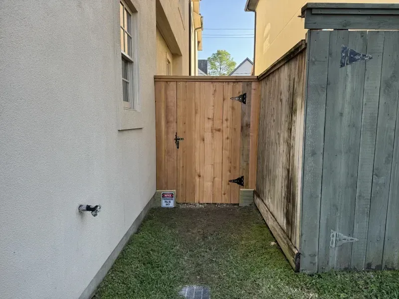 Wooden gate between two buildings, opening to a grassy yard.