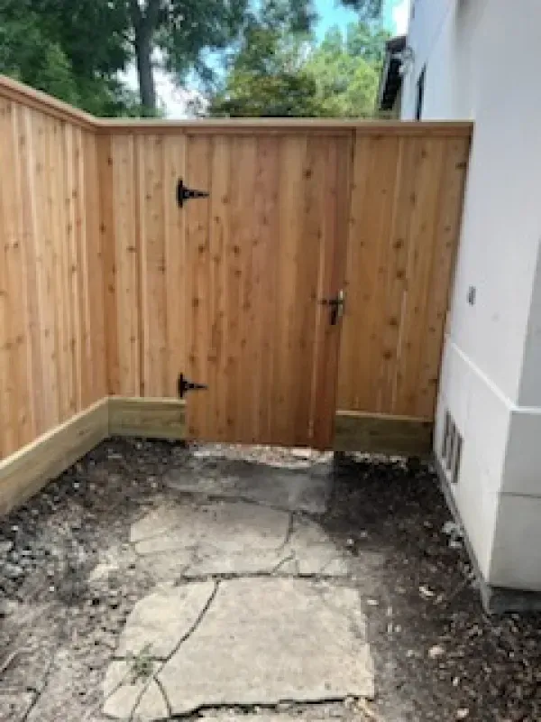 Wooden fence with gate, leading to a pathway with cracked concrete.