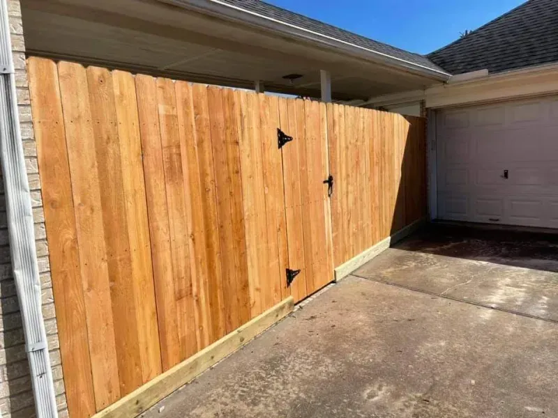 Wooden fence with a gate, next to a garage, under a house's roof.