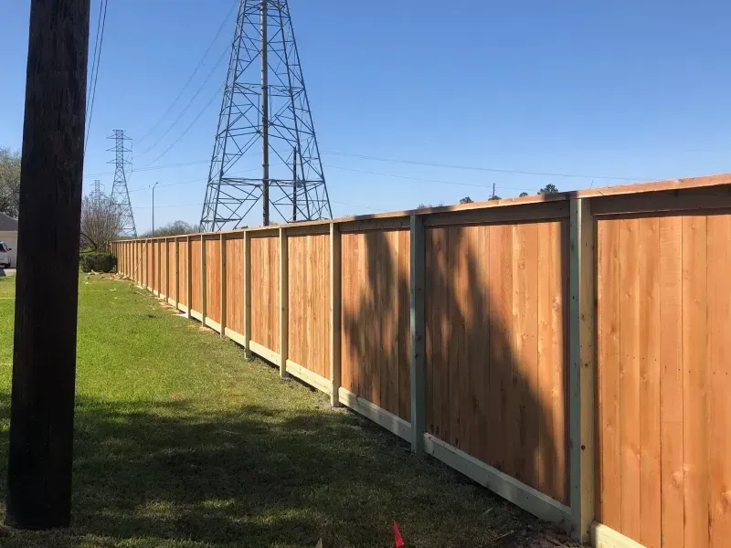 Wooden fence along a grassy area, with power lines and blue sky in the background.