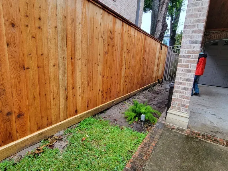 Wooden fence alongside a brick building, person in red jacket in the background.