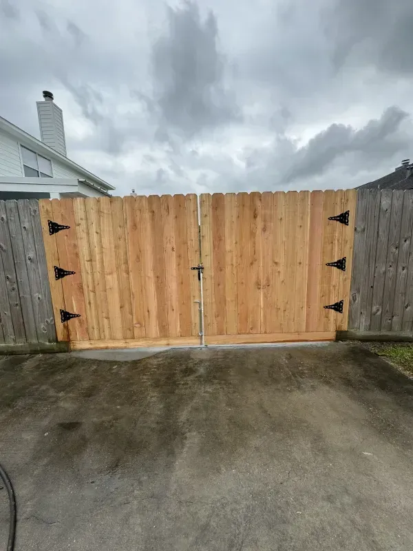 Wooden double gate, light brown, set in concrete, against a cloudy sky.