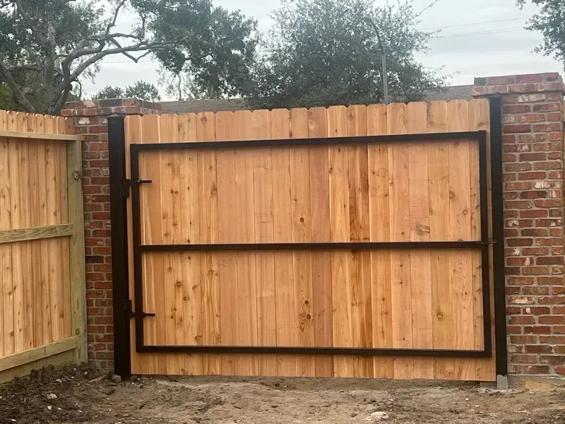 Wooden gate with a black metal frame set in a brick and wooden fence.