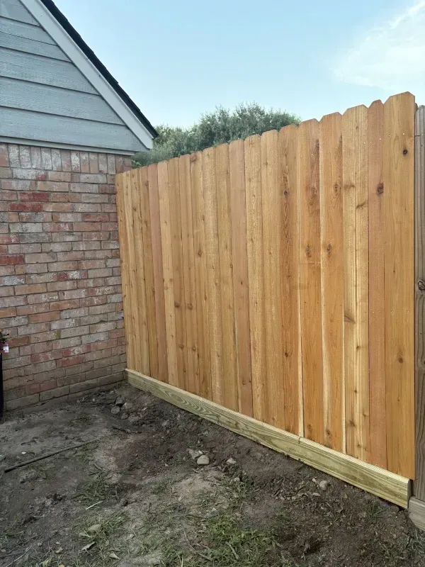 Wooden fence next to a brick wall and a house with blue siding.