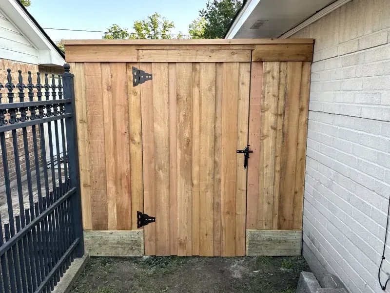 Wooden gate with black hardware and a latch, set between a brick wall and a fence.