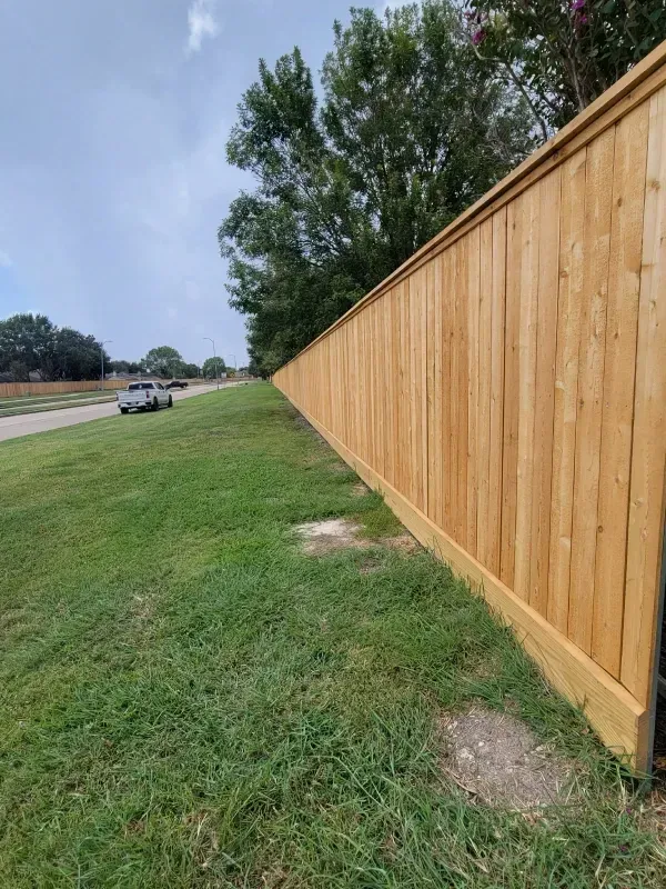 Wooden fence along a grassy lawn, with a road and a vehicle visible in the distance.