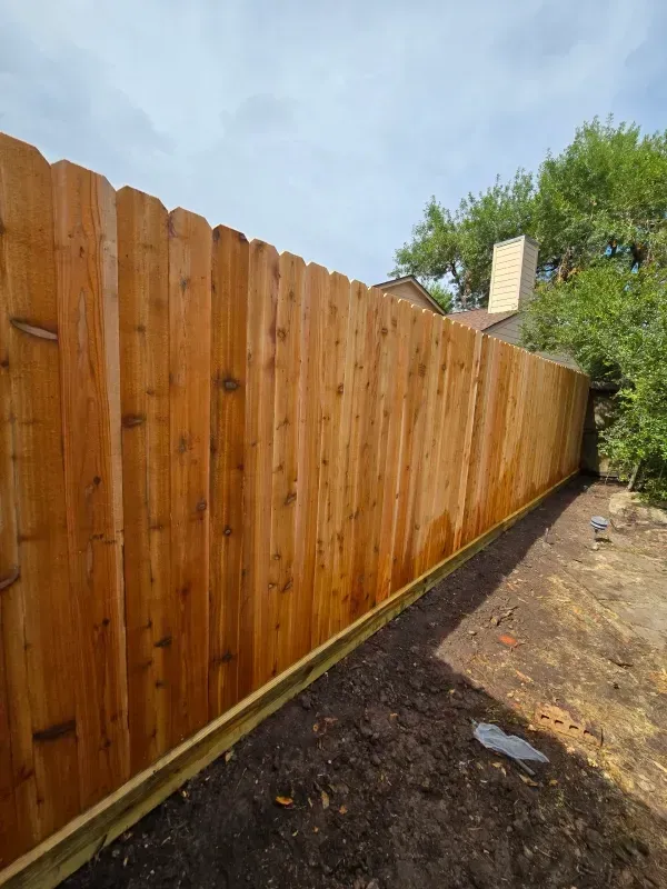 Wooden fence in a yard with a slightly overcast sky, dirt ground.