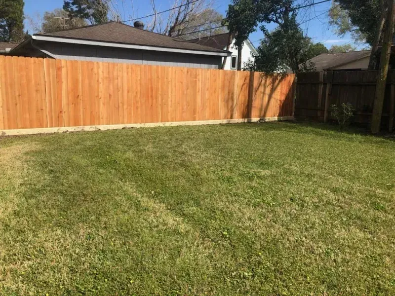 A backyard with a wooden fence and grass lawn under a clear blue sky.