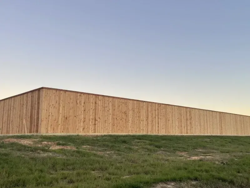 Long wooden fence on grassy hill under a clear blue and yellow sky.